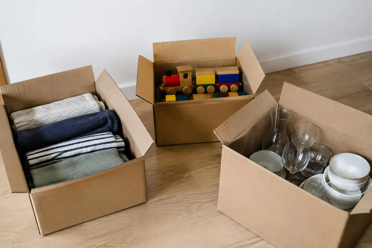 Tres cajas abiertas en el piso con ropa doblada, un tren de madera y cristalería organizados